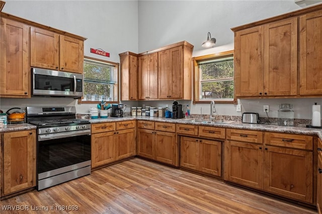 11667 Falling Rock Rd, Havana, AR 72842 - kitchen featuring stainless steel appliances, brown cabinetry, light wood-style floors, and a high ceiling