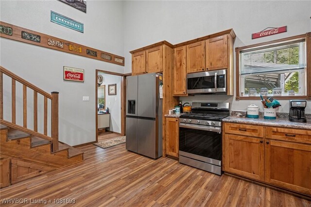 11667 Falling Rock Rd, Havana, AR 72842 - kitchen with stainless steel appliances, a towering ceiling, light wood finished floors, and brown cabinetry