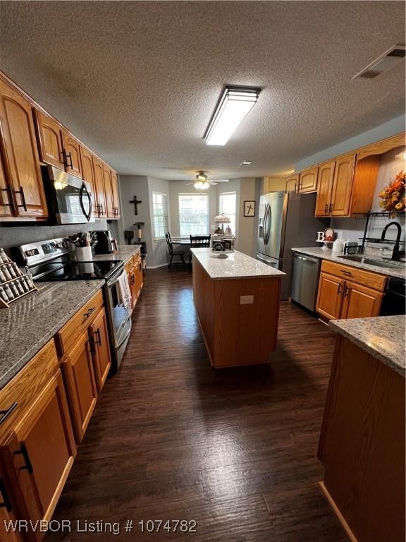 kitchen with a center island, sink, ceiling fan, a textured ceiling, and stainless steel appliances