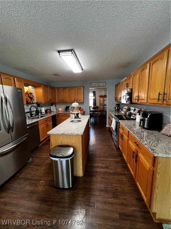 kitchen with dark hardwood / wood-style flooring, a textured ceiling, stainless steel appliances, sink, and a kitchen island