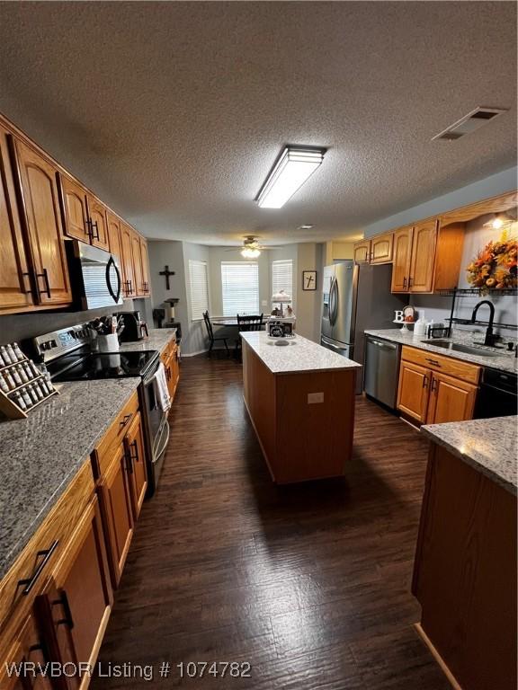 kitchen featuring a textured ceiling, stainless steel appliances, sink, a center island, and dark hardwood / wood-style floors