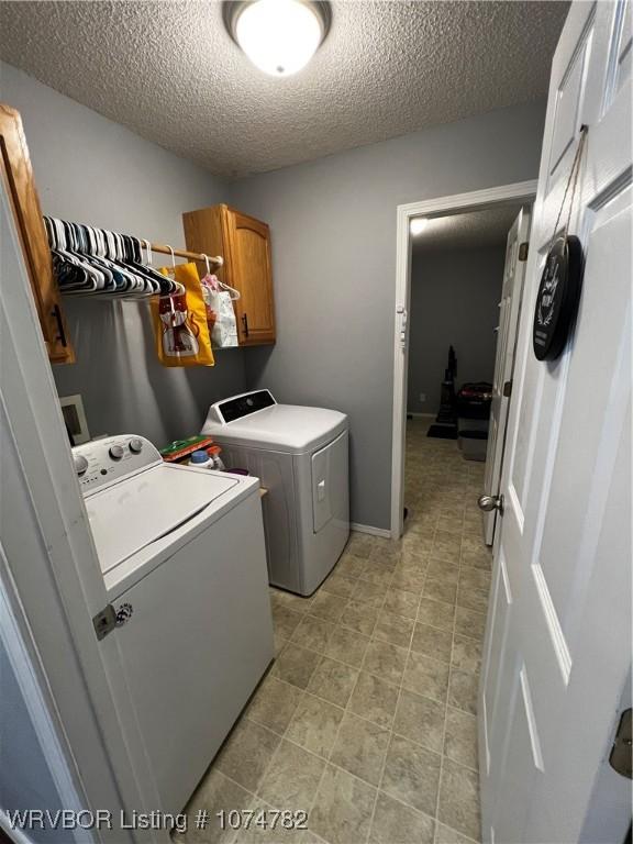 clothes washing area with washer and clothes dryer, cabinets, and a textured ceiling