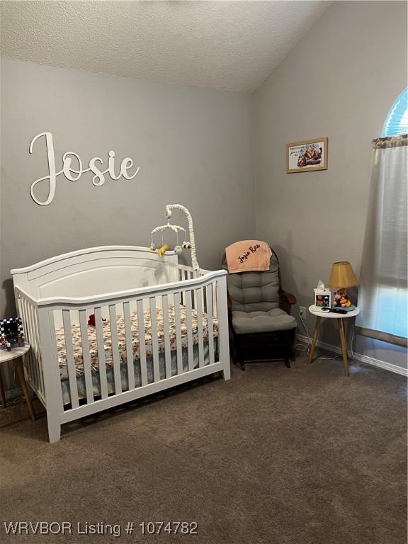 bedroom with dark colored carpet, a textured ceiling, vaulted ceiling, and a nursery area