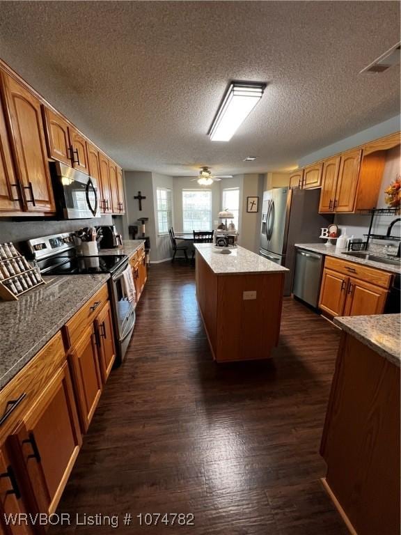 kitchen with a textured ceiling, stainless steel appliances, ceiling fan, sink, and a center island