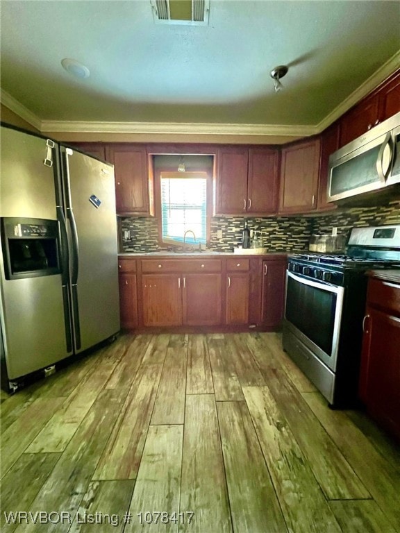 kitchen featuring light wood-type flooring, stainless steel appliances, ornamental molding, and sink