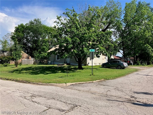 view of property hidden behind natural elements featuring a front yard and fence