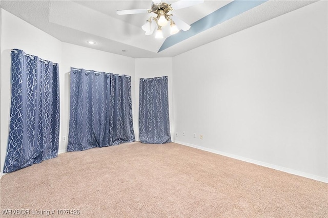 spare room with ceiling fan, carpet floors, and a tray ceiling