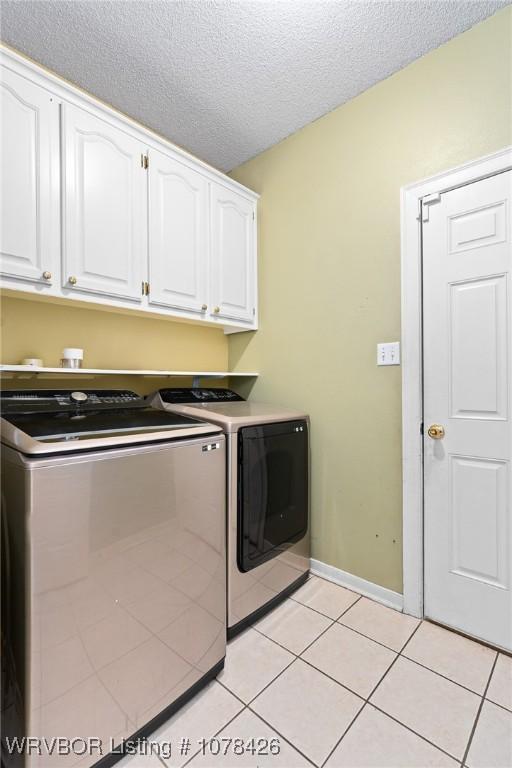 laundry room featuring cabinets, a textured ceiling, light tile patterned floors, and washing machine and clothes dryer