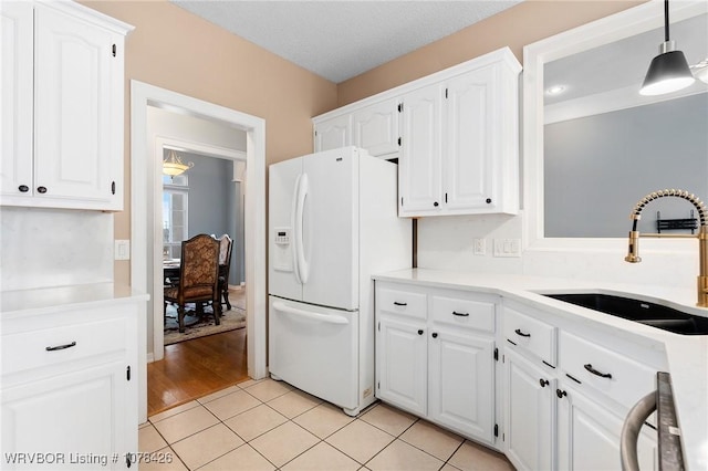 kitchen featuring light tile patterned floors, white cabinetry, white fridge with ice dispenser, pendant lighting, and sink