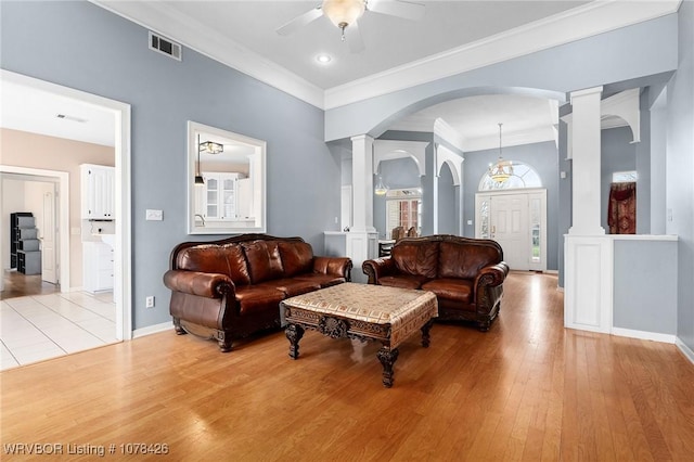 living room with light wood-type flooring, ceiling fan, ornamental molding, and decorative columns