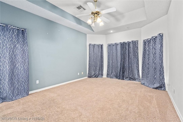 carpeted spare room with ceiling fan and a raised ceiling