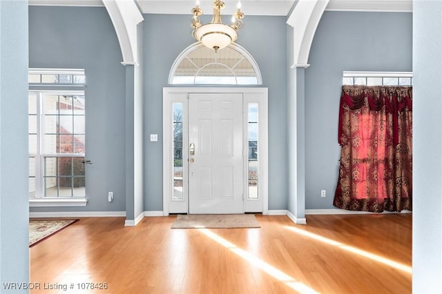 entryway with a healthy amount of sunlight, a towering ceiling, an inviting chandelier, and hardwood / wood-style floors