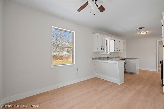 kitchen with light wood finished floors, a peninsula, light countertops, white cabinetry, and a sink