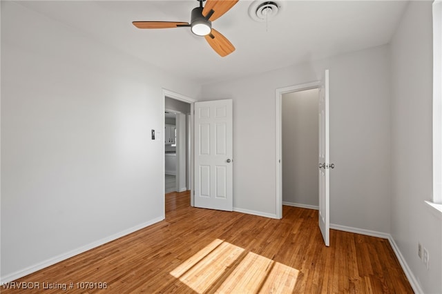 unfurnished bedroom featuring a ceiling fan, visible vents, baseboards, and wood finished floors