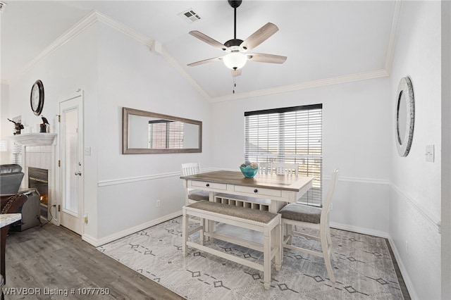 dining room featuring ceiling fan, light hardwood / wood-style flooring, lofted ceiling, a fireplace, and ornamental molding