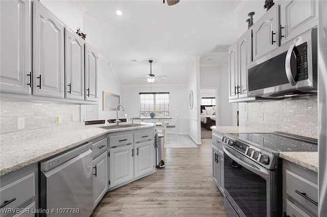 kitchen featuring sink, ceiling fan, ornamental molding, appliances with stainless steel finishes, and light stone counters