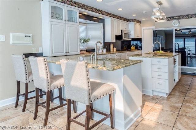 kitchen featuring decorative backsplash, light stone counters, a center island with sink, and decorative light fixtures