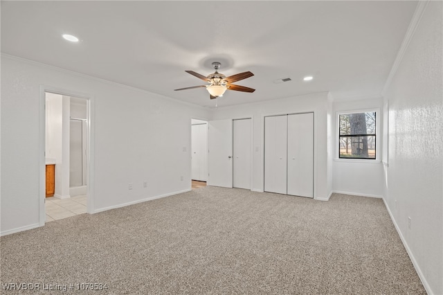 unfurnished bedroom featuring visible vents, light carpet, two closets, and crown molding