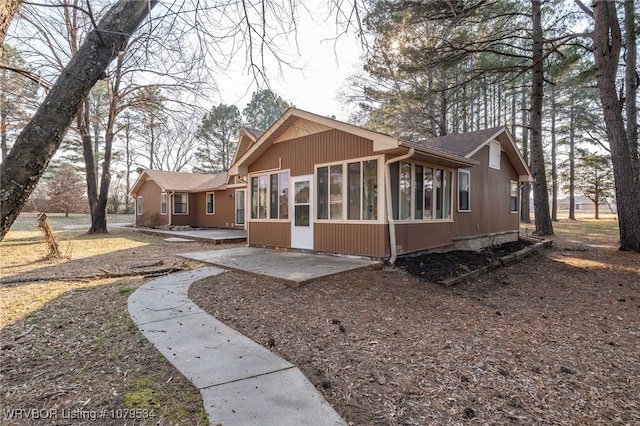 back of house with roof with shingles, a patio, and a sunroom