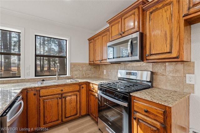 kitchen with a sink, stainless steel appliances, brown cabinets, and ornamental molding