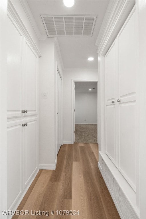 corridor with visible vents, ornamental molding, baseboards, and wood finished floors