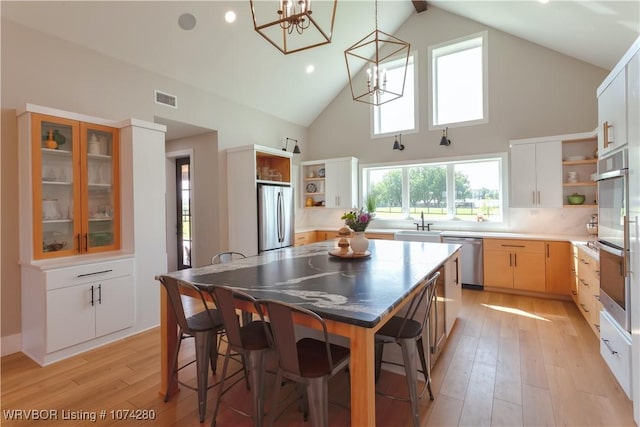 kitchen featuring stainless steel appliances, a kitchen island, high vaulted ceiling, light hardwood / wood-style floors, and white cabinets