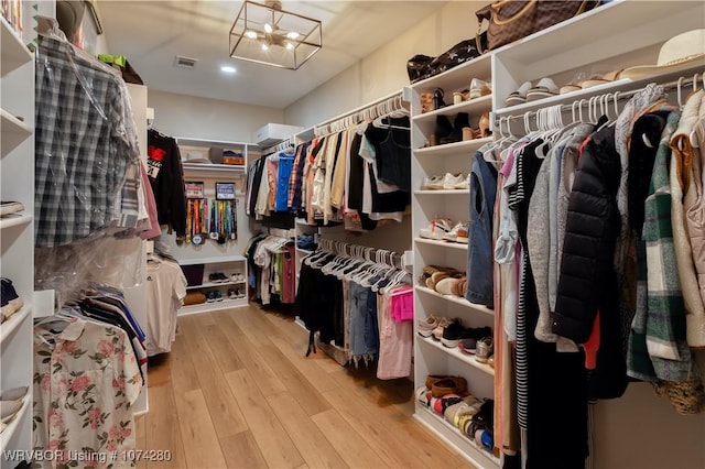 spacious closet featuring light hardwood / wood-style flooring and an inviting chandelier