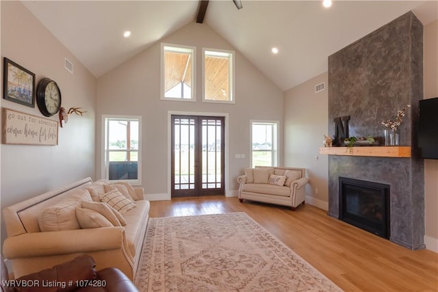 living room featuring high vaulted ceiling, french doors, light wood-type flooring, a fireplace, and beam ceiling