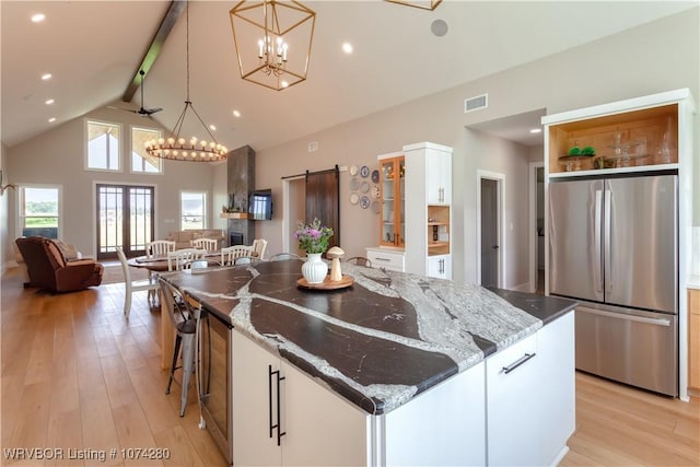 kitchen with dark stone counters, white cabinets, hanging light fixtures, a large island, and stainless steel refrigerator