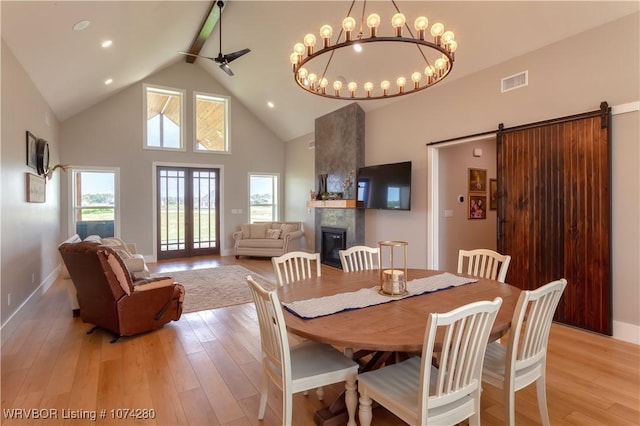 dining room featuring beam ceiling, a barn door, light hardwood / wood-style flooring, high vaulted ceiling, and ceiling fan with notable chandelier