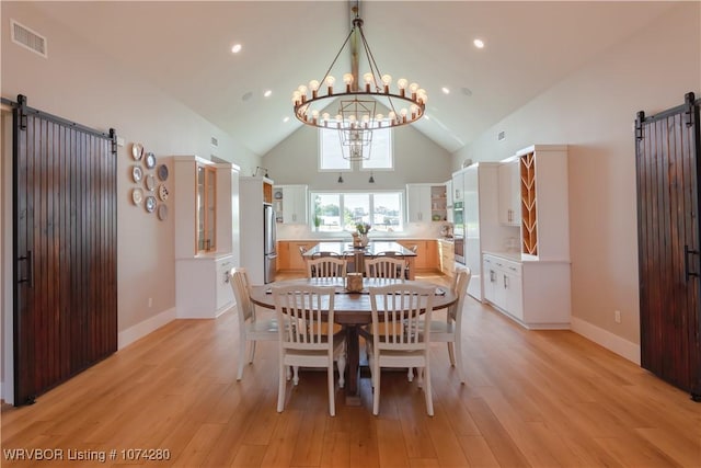 dining room featuring a barn door, high vaulted ceiling, light hardwood / wood-style floors, and an inviting chandelier