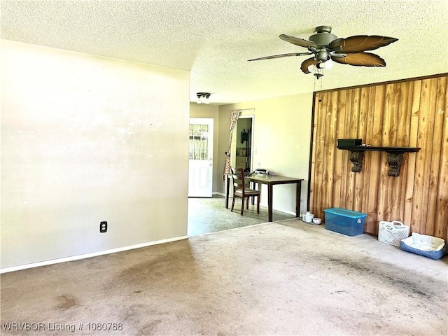carpeted spare room with a textured ceiling, wood walls, baseboards, and a ceiling fan