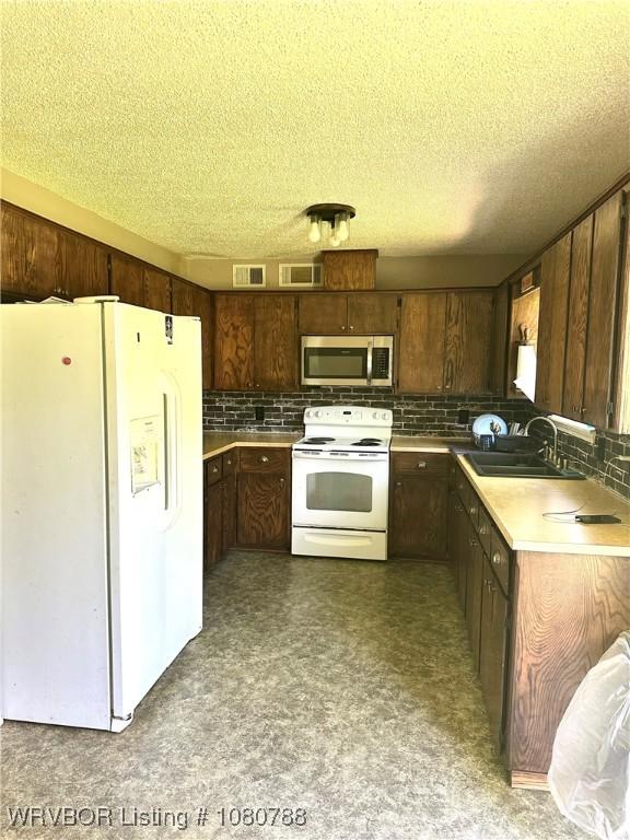 kitchen with a sink, a textured ceiling, visible vents, white appliances, and tasteful backsplash