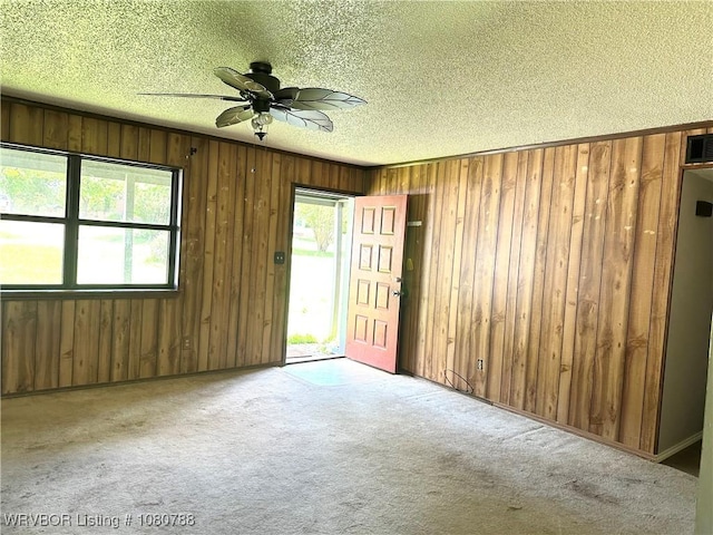 spare room with carpet, a textured ceiling, wooden walls, and a ceiling fan