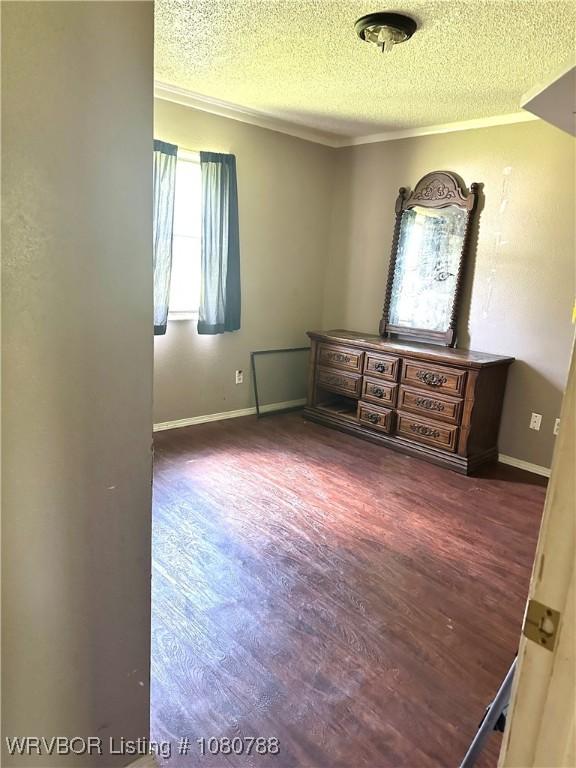 empty room featuring crown molding, a textured ceiling, baseboards, and dark wood-type flooring