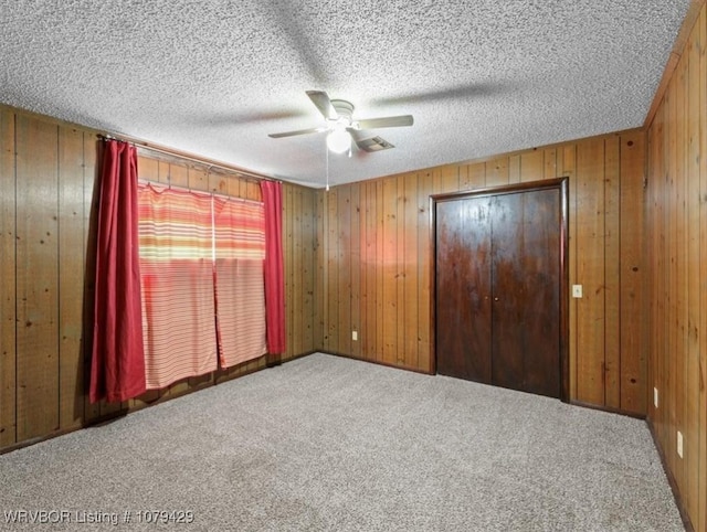 unfurnished bedroom with wooden walls, a textured ceiling, a ceiling fan, and carpet floors