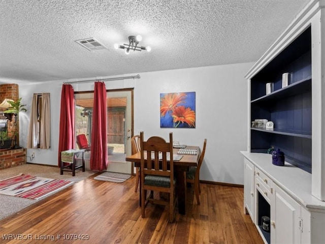 dining room featuring visible vents, a notable chandelier, a textured ceiling, wood finished floors, and baseboards