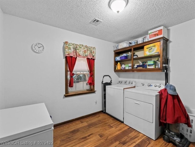 laundry area featuring wood finished floors, visible vents, washing machine and clothes dryer, laundry area, and a textured ceiling