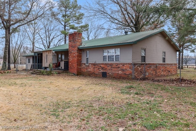 exterior space featuring fence, a yard, metal roof, brick siding, and a chimney