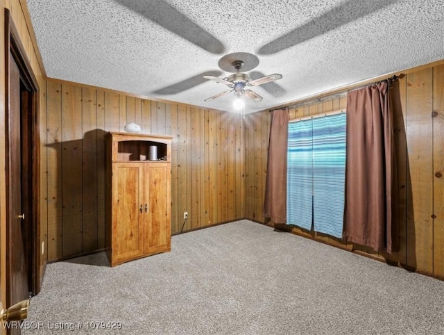 interior space featuring a ceiling fan, carpet, wood walls, and a textured ceiling