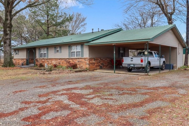 view of front of home featuring an attached carport, brick siding, driveway, and metal roof