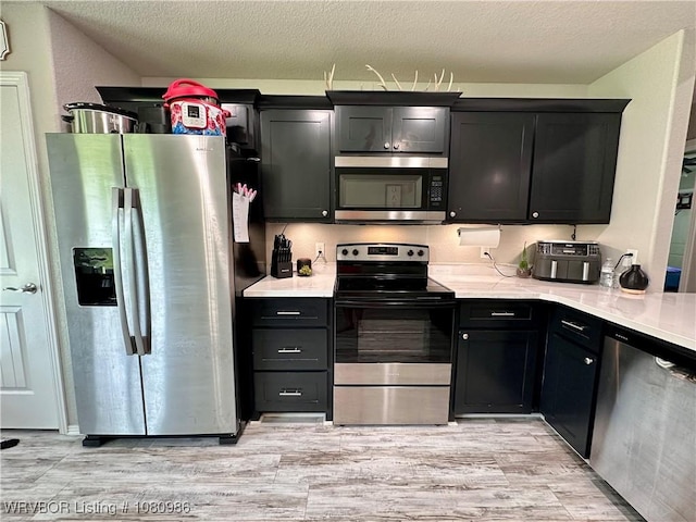 309 Arcadia Dr, Poteau, OK 74953 - kitchen with stainless steel appliances, light countertops, light wood-type flooring, dark cabinetry, and a textured ceiling