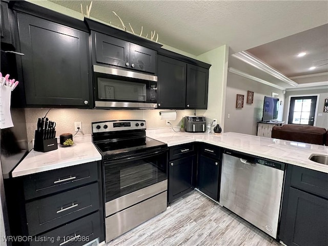 309 Arcadia Dr, Poteau, OK 74953 - kitchen featuring stainless steel appliances, light wood-type flooring, dark cabinets, ornamental molding, and a tray ceiling