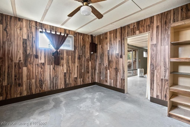 empty room with ceiling fan, concrete flooring, and wooden walls