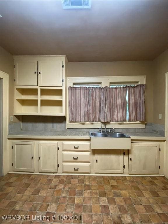 kitchen featuring open shelves, backsplash, light countertops, visible vents, and a sink