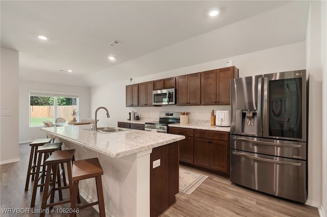 10618 Cedar Way, Fort Smith, AR 72916 - kitchen with stainless steel appliances, a kitchen island with sink, light wood-style floors, a breakfast bar area, and dark brown cabinets
