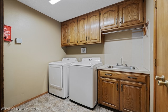 clothes washing area featuring washing machine and clothes dryer, cabinet space, baseboards, and a sink