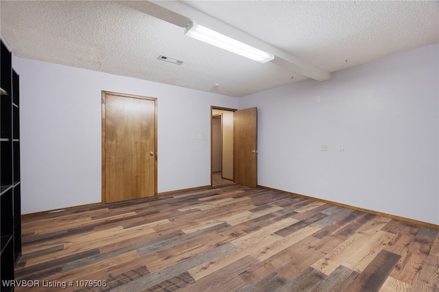 unfurnished room featuring baseboards, wood finished floors, visible vents, and a textured ceiling