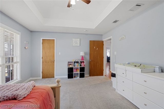 bedroom with visible vents, light colored carpet, and a tray ceiling