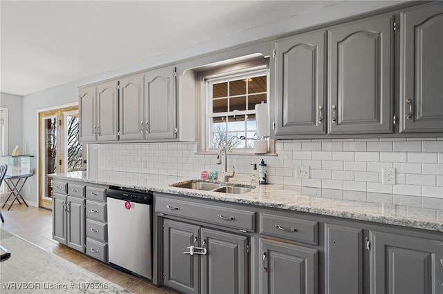 kitchen with gray cabinetry, a sink, tasteful backsplash, dishwashing machine, and light stone countertops